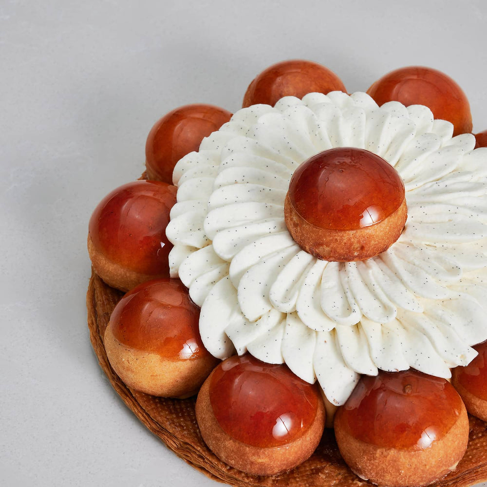 A close up of a classic Vanilla Saint Honore cake with Madagascar vanilla cream piping and caramel-capped choux puffs