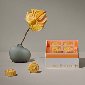 4 salted egg custard mooncakes inside a 2022 mooncake gift set in gradient orange with 2 salted egg mooncakes on the table and a vase with a yellow flower by its side