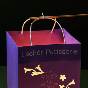 A close up of a stick tied to the handles of a lighted paper bag lantern.