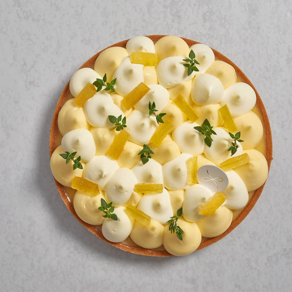 The top view of a citron tart piped with lemon cream and white chantilly cream, garnished by rectangular lemon peel and green lemon thyme