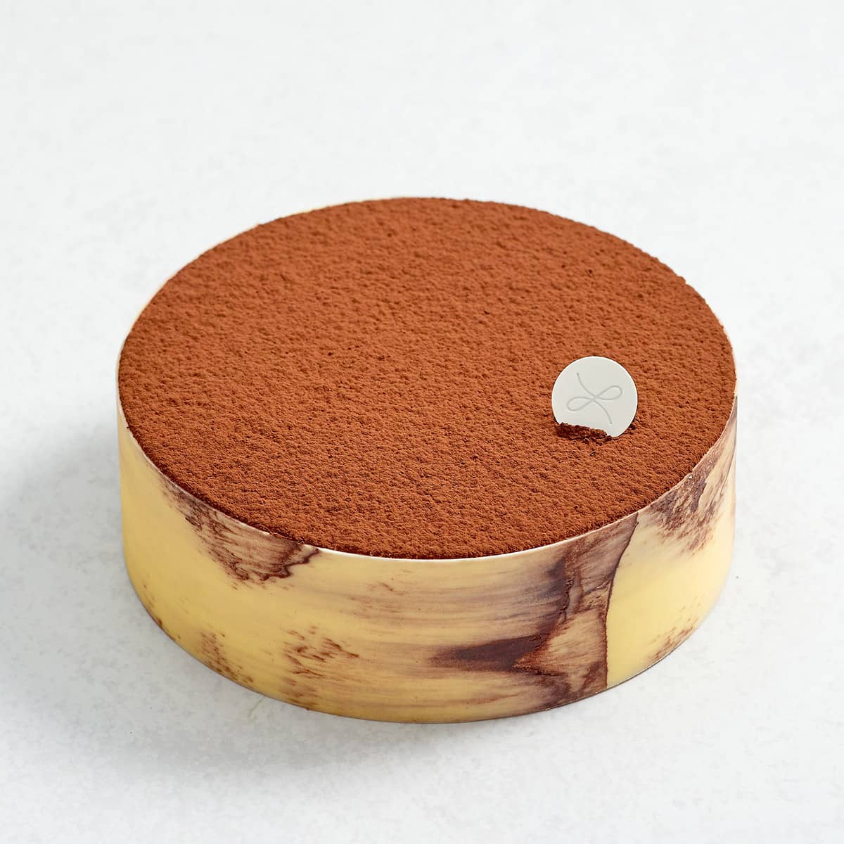 A classic tiramisu cake with a white chocolate collar dusted in cocoa powder with a lacher patisserie logo insert.